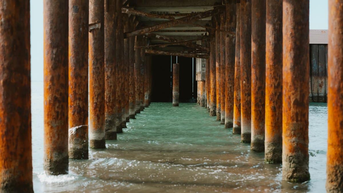 Underneath view of a rustic pier in Baku, showcasing aged wooden beams over clear water.