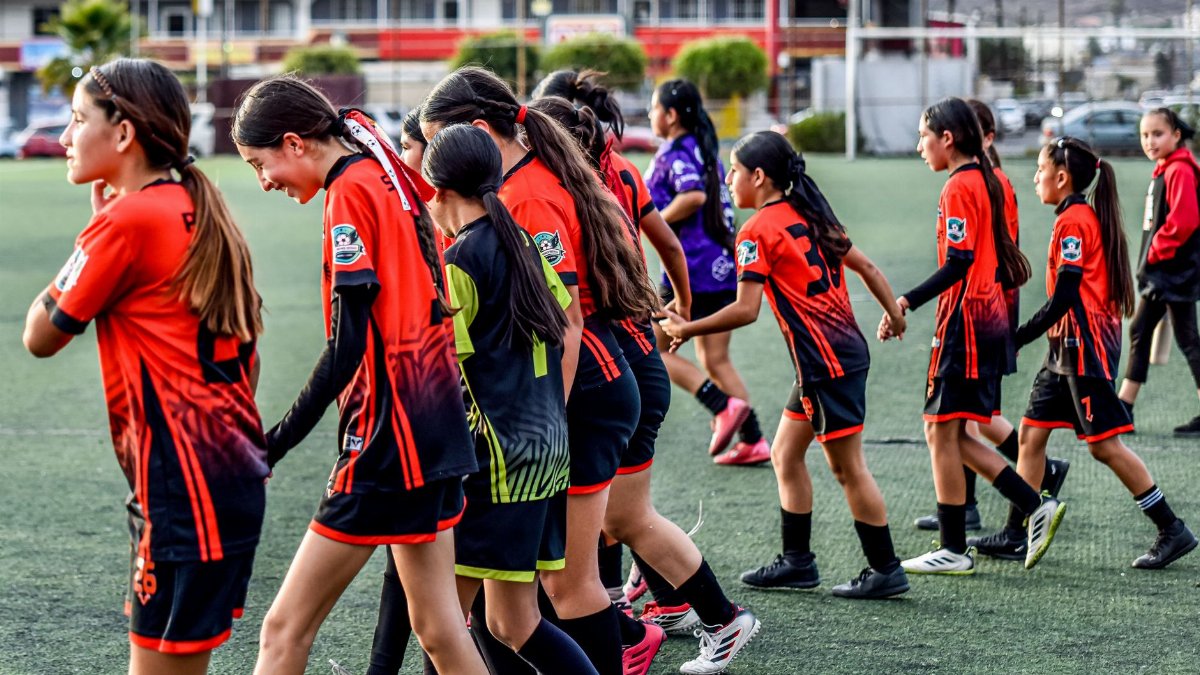 A group of young girls in soccer uniforms warming up together on a field.