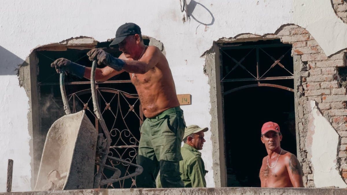 Three construction workers labor on a building renovation site on a sunny day.