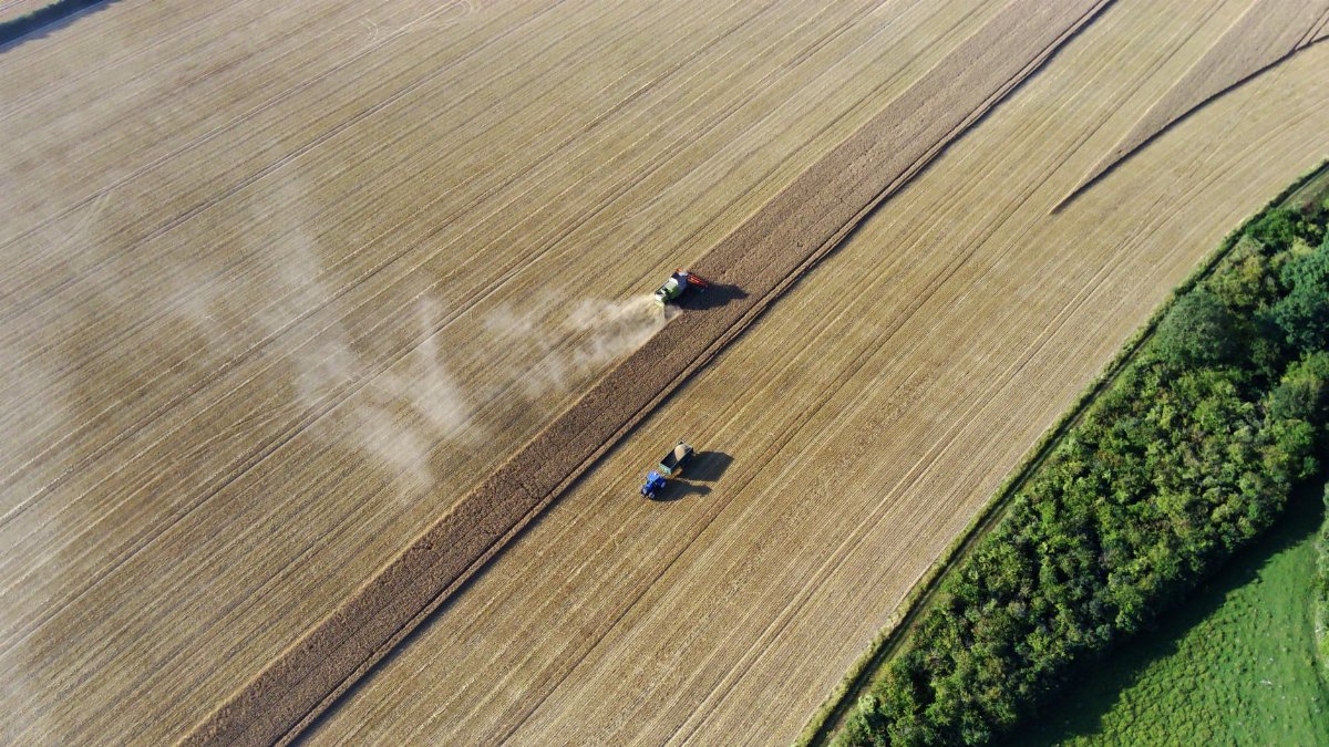 Aerial drone shot of tractors working field in Sharpenhoe, England, during harvest season.
