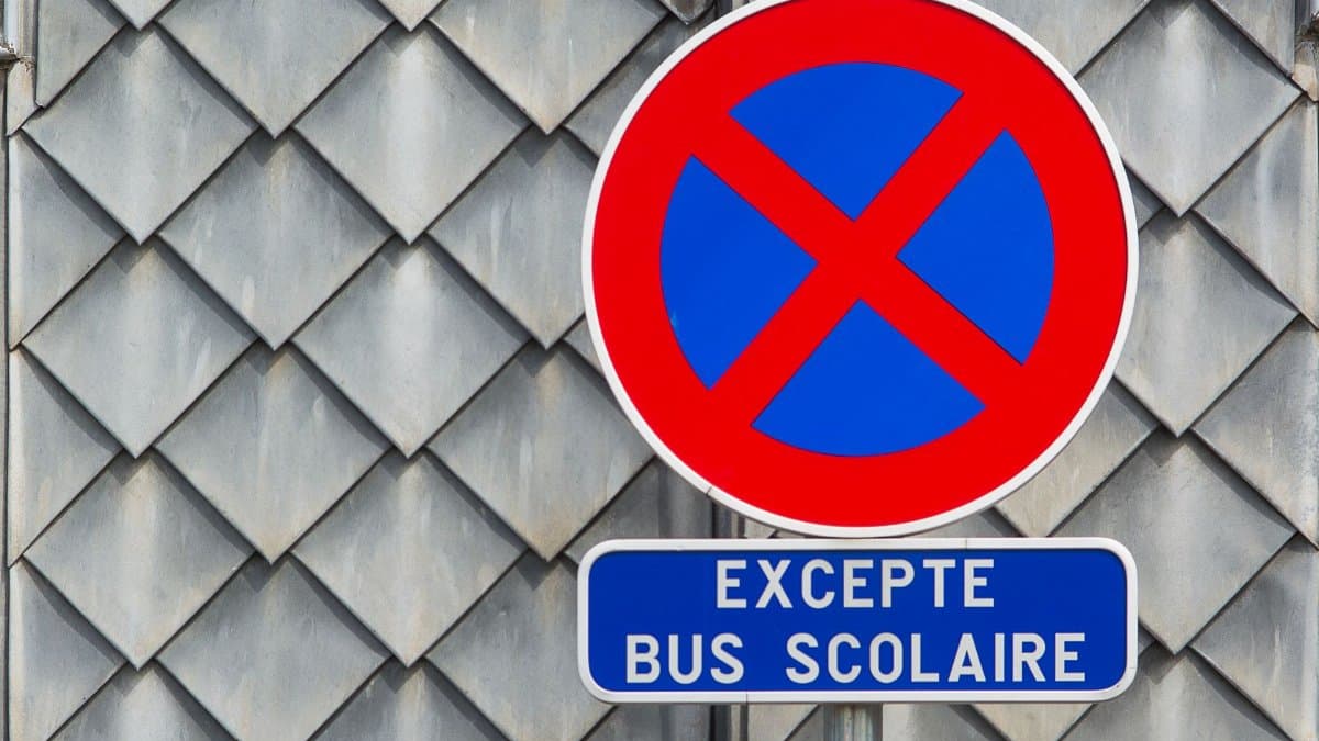 Close-up of a French no parking sign with a school bus exception on a tiled building facade.