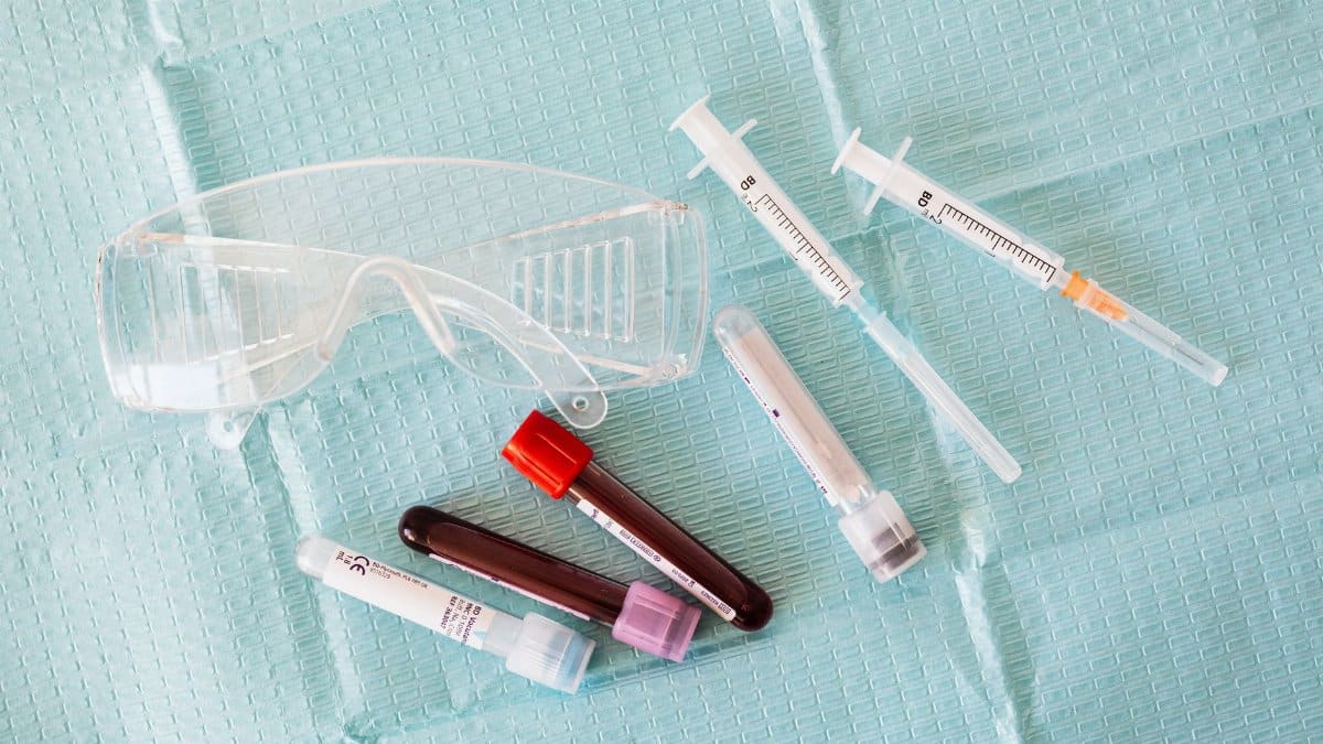 Top view of empty and full of blood vials and plastic syringes and eyeglasses placed on medical diaper