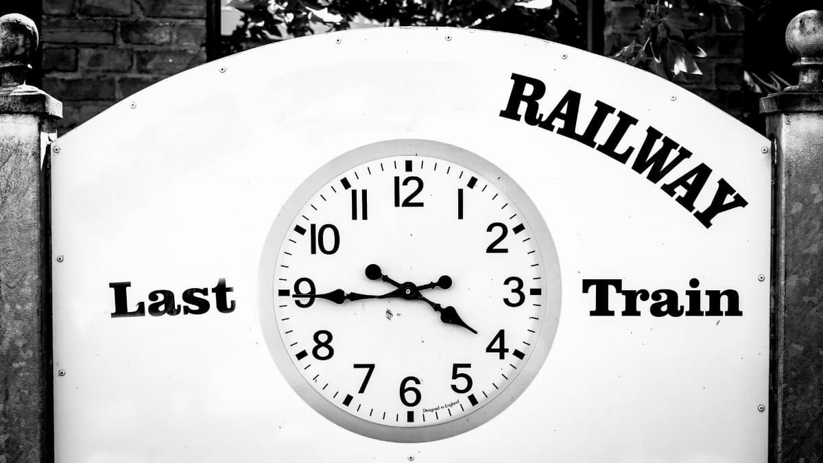 Black and white image of a wall clock with 'Last Train' at a railway station sign.