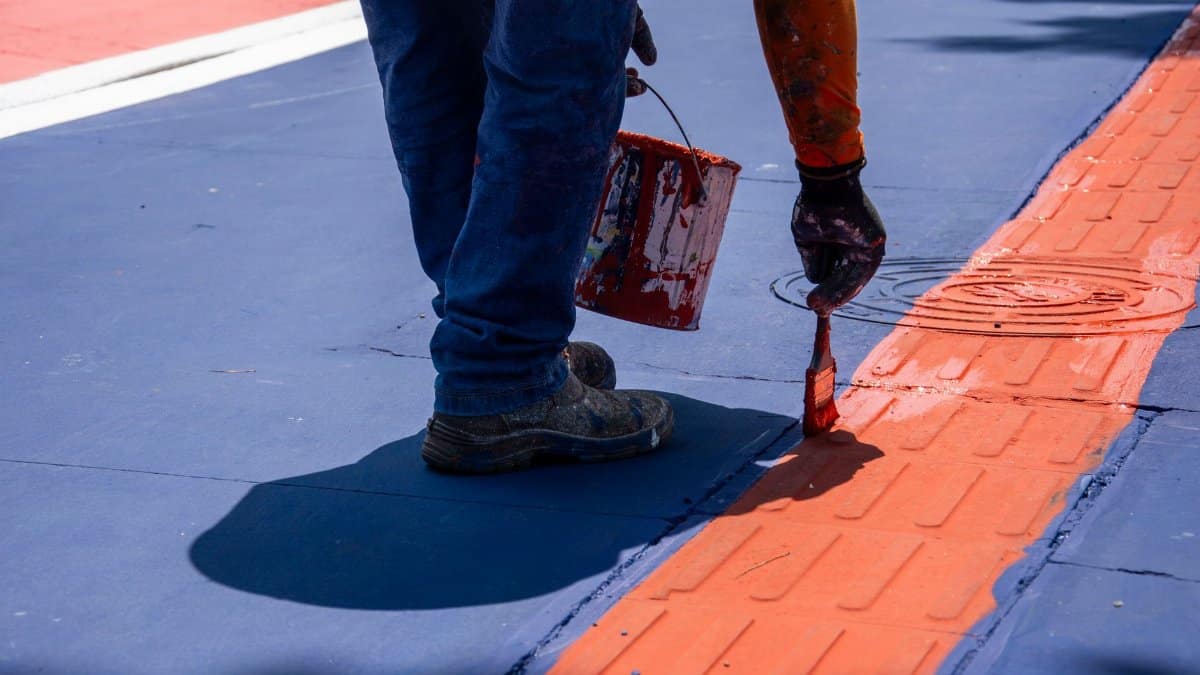 A person paints a red line on a city street, adding vibrant color to the environment.