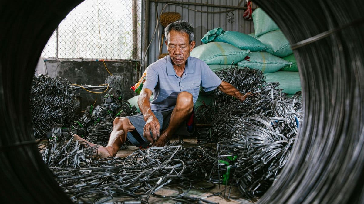 Elderly man organizing electrical wires in a workshop, surrounded by industrial materials.