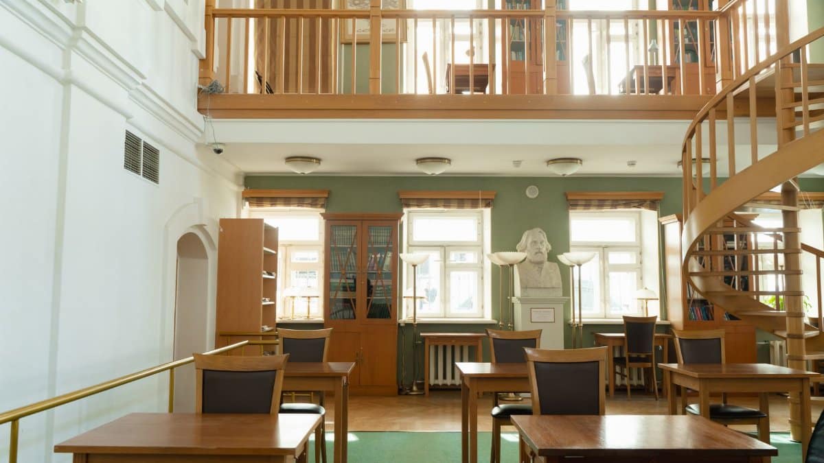 Spacious library interior featuring wooden tables and spiral staircase under natural light.
