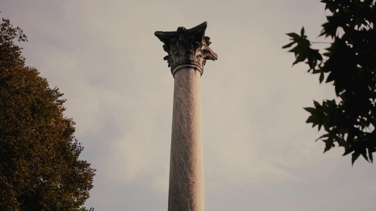 Majestic ancient stone column surrounded by trees under a clear sky.