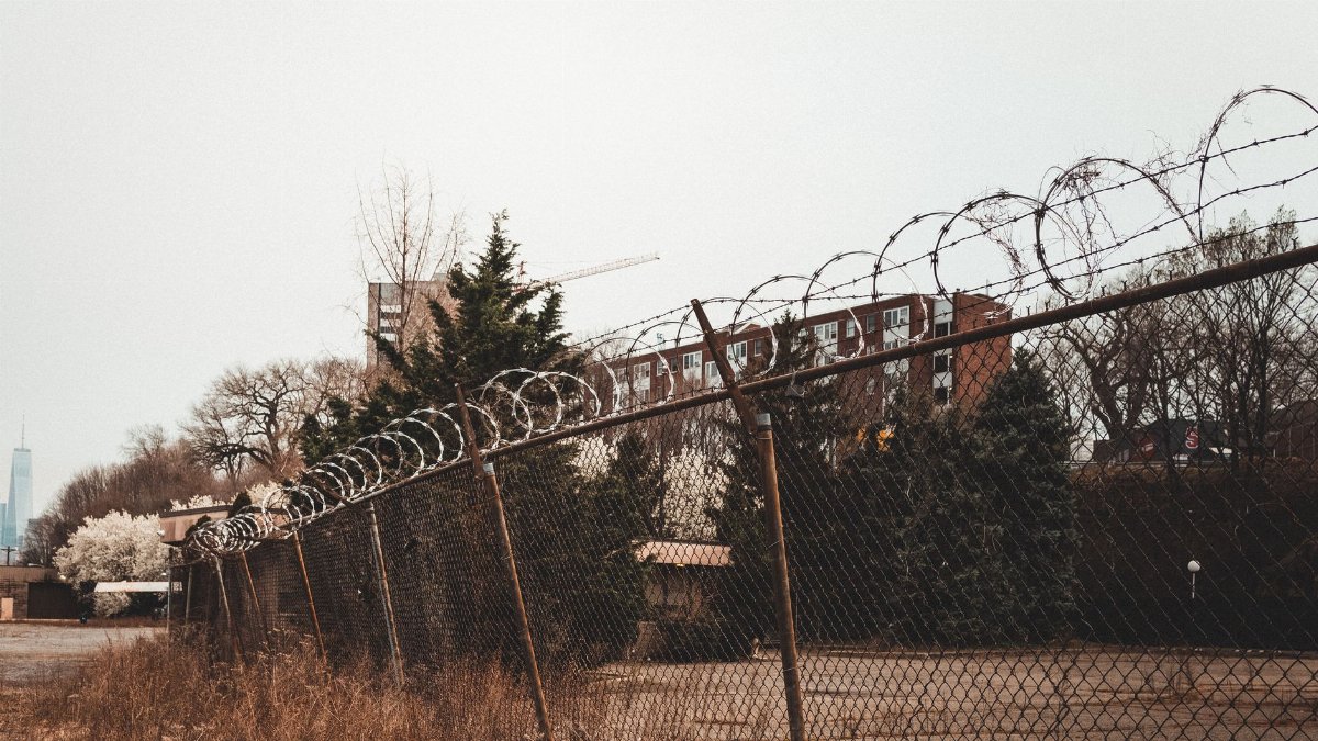A rusty barbed wire fence with cityscape in the background, showcasing urban security in Hoboken, NJ.