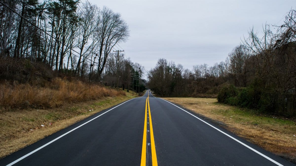A deserted rural road stretches through a bare winter landscape, offering a peaceful and solitary scene.
