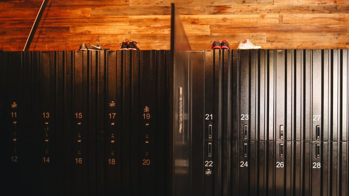 Stylish locker room in gym with wooden walls and steel black lockers with sneakers placed on roof of lockers divided by partition
