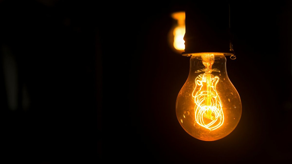 Close-up view of an illuminated vintage light bulb with glowing filament against a dark background.