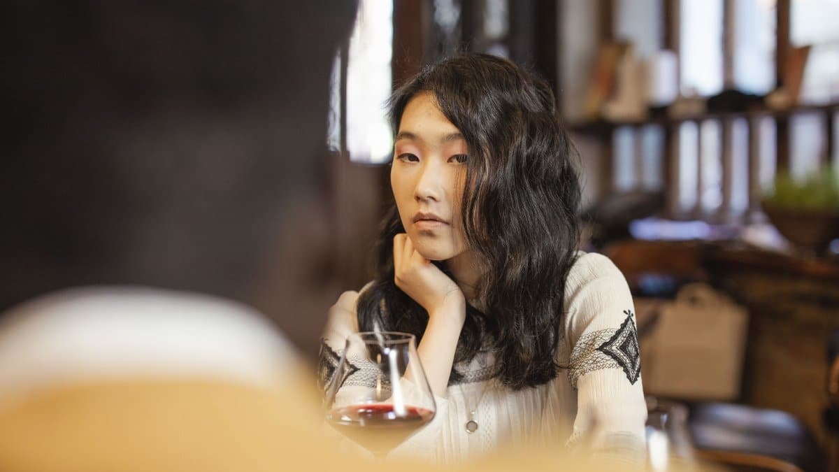 Serene young woman reflecting while enjoying a glass of wine in a cozy indoor setting.