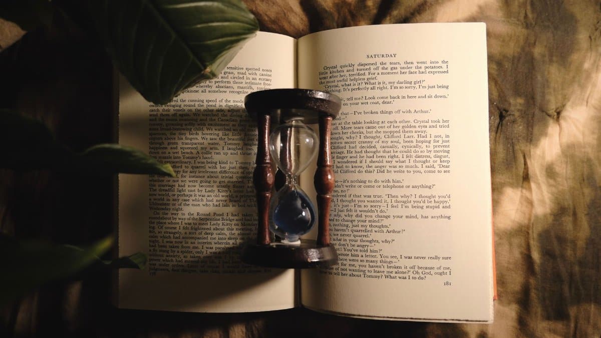 A vintage hourglass sits on an open book, casting intriguing shadows under warm light.