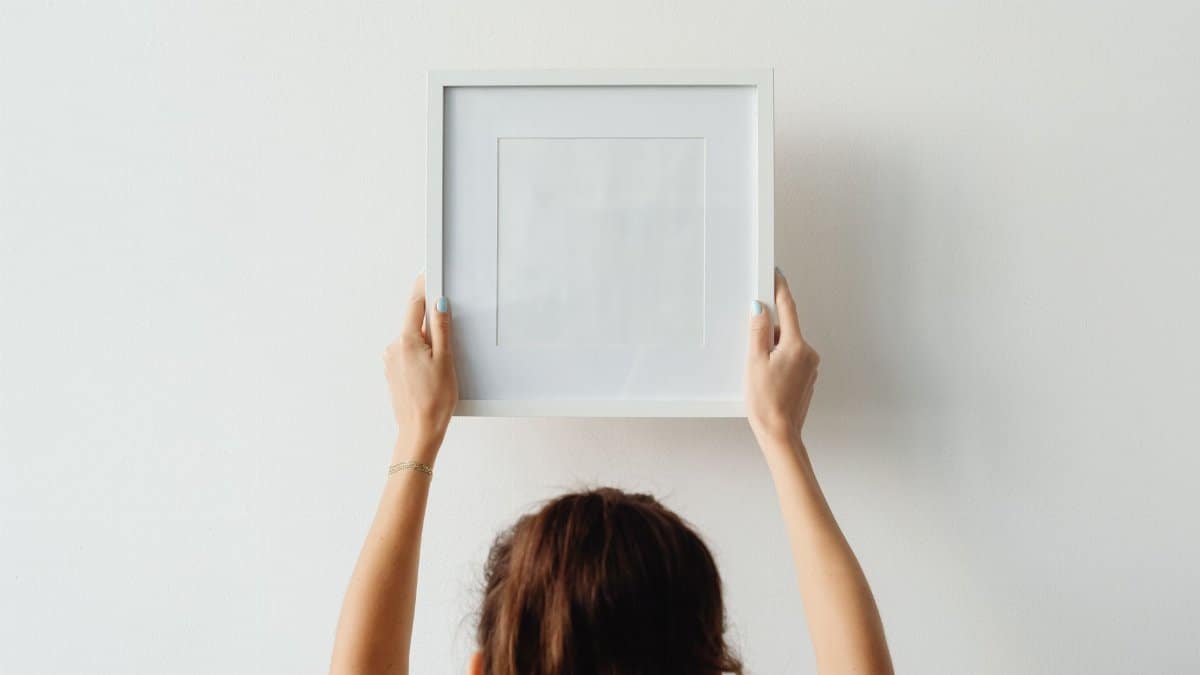 A woman hangs an empty frame on a white wall with copy space.