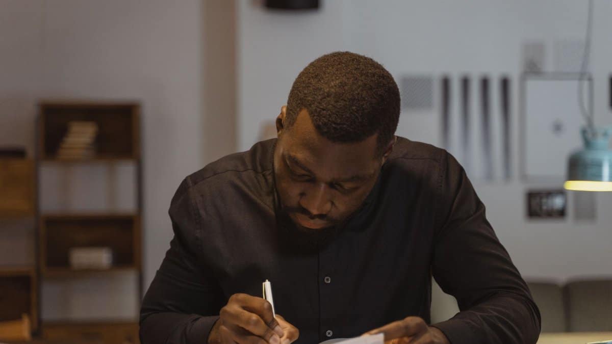 A man diligently writing notes in a modern office environment. Perfect for business and productivity themes.