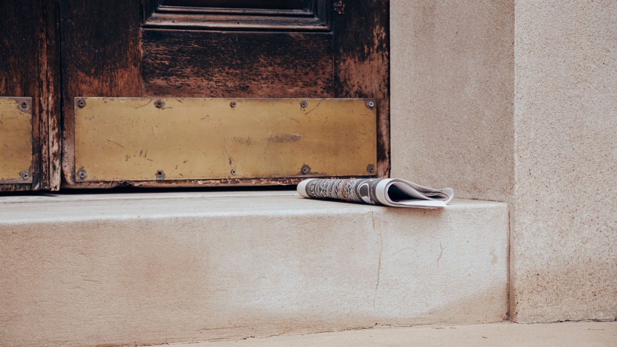 Folded newspaper on a stone step in front of a classic wooden door, urban street scene.