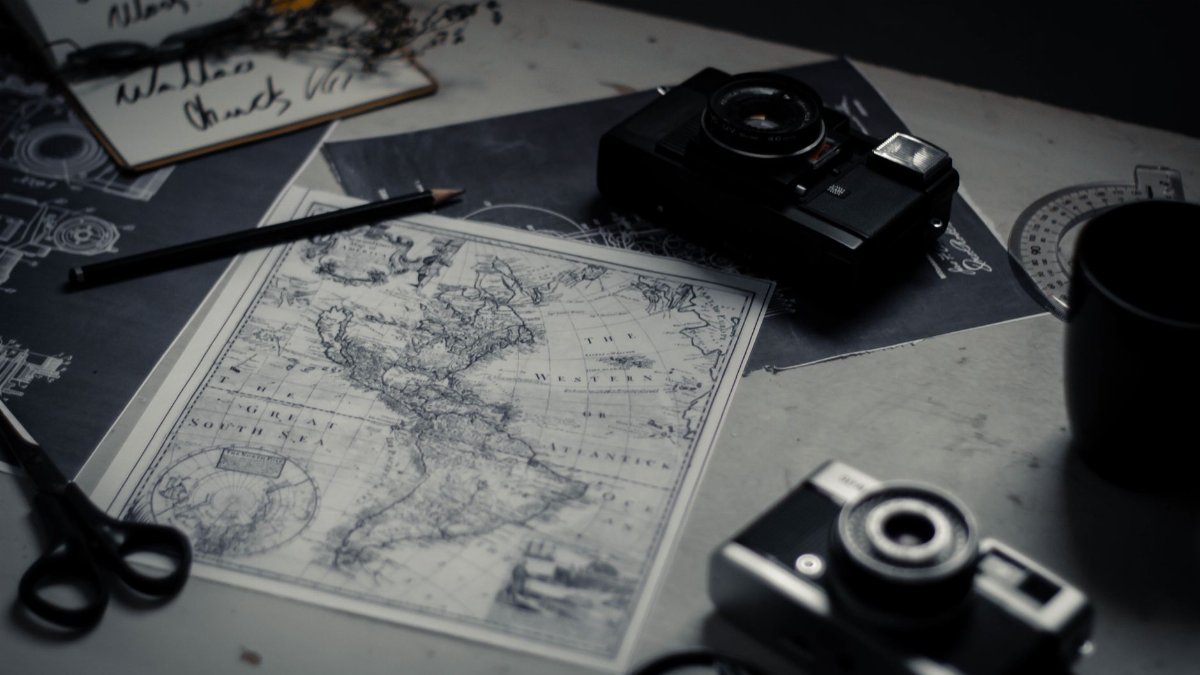 Electronic devices for taking photo and scissors with pencil composing with herbarium and detailed map of world on table in room