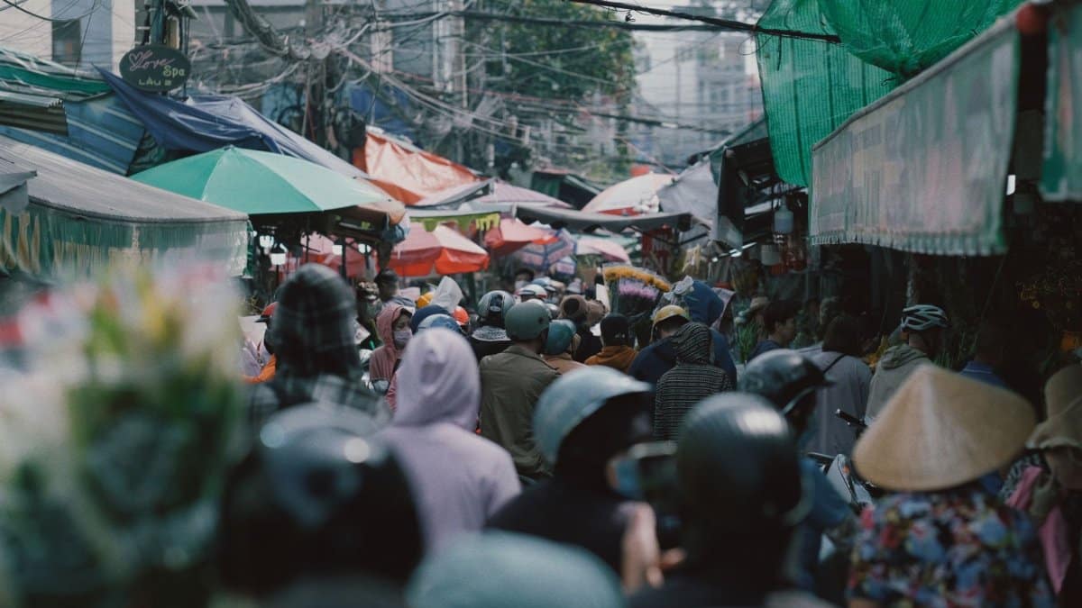 Bustling outdoor market scene with diverse vendors and shoppers under colorful canopies.