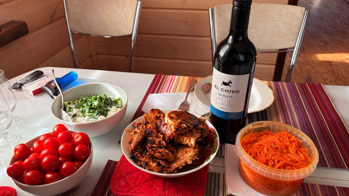 A cozy indoor table setting with wine, fresh tomatoes, and grilled chicken ready for a delightful meal.