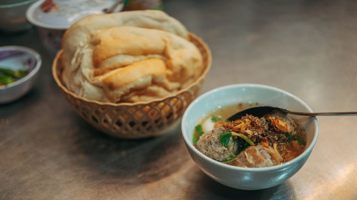 A flavorful bowl of meatball soup paired with fresh bread on a stainless steel counter.
