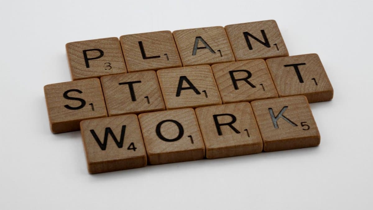 Wooden Scrabble tiles spelling 'Plan', 'Start', 'Work' on a white background.