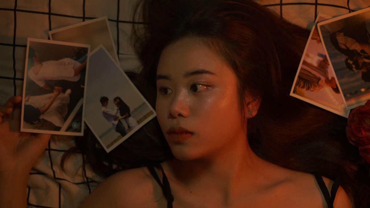 Asian woman on bed surrounded by nostalgic photographs. Top view.
