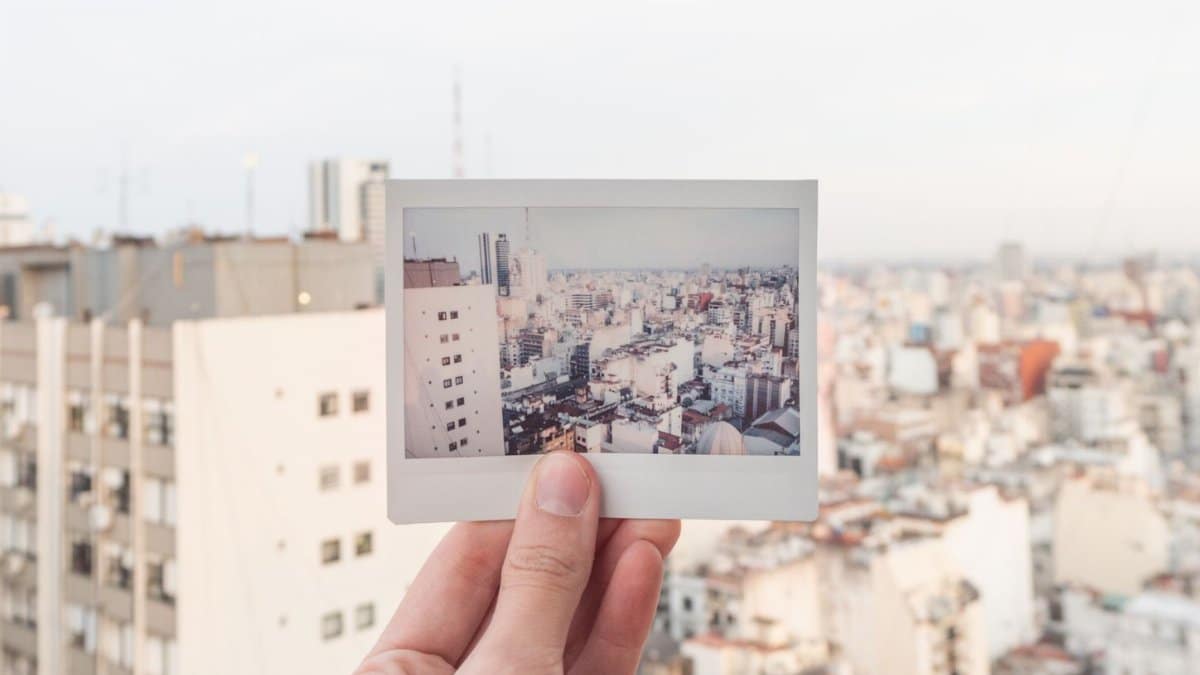 A hand holds a Polaroid of a city skyline against a blurred urban backdrop.