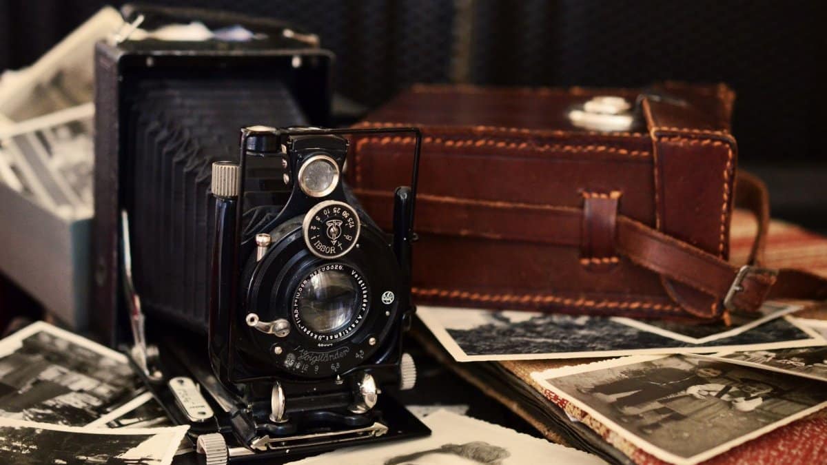 Classic black vintage camera with old photographs and a leather case, displaying nostalgic charm.