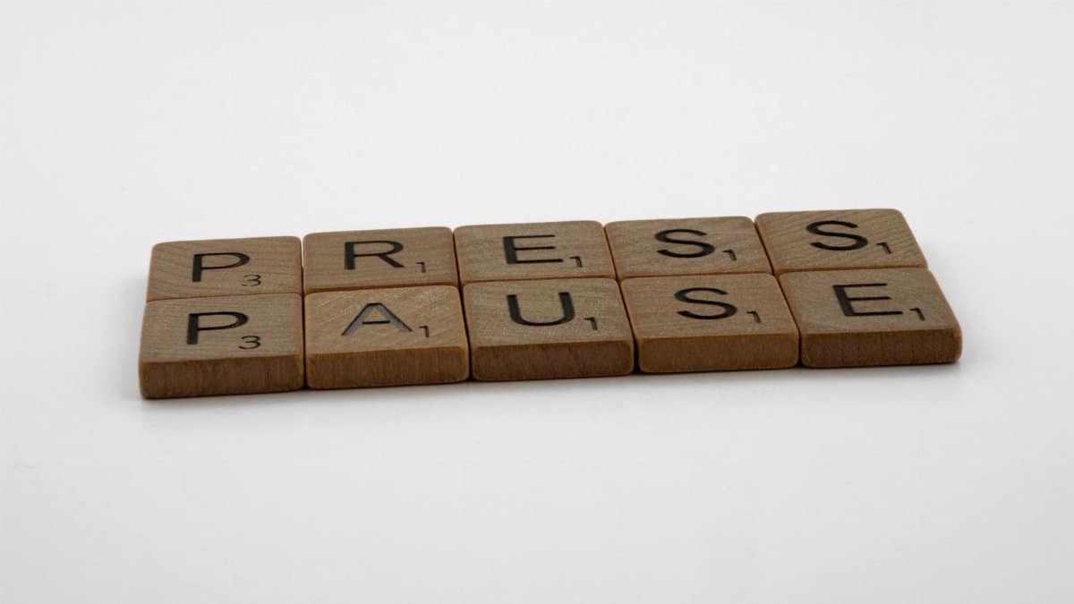 Wooden Scrabble tiles arranged to spell 'Press Pause' on a clean white background.