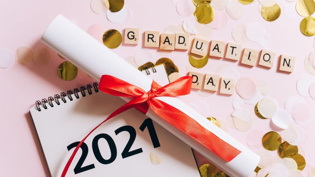 A celebratory graduation scene featuring a diploma, 2021 calendar, and Scrabble tiles spelling 'graduation day'.