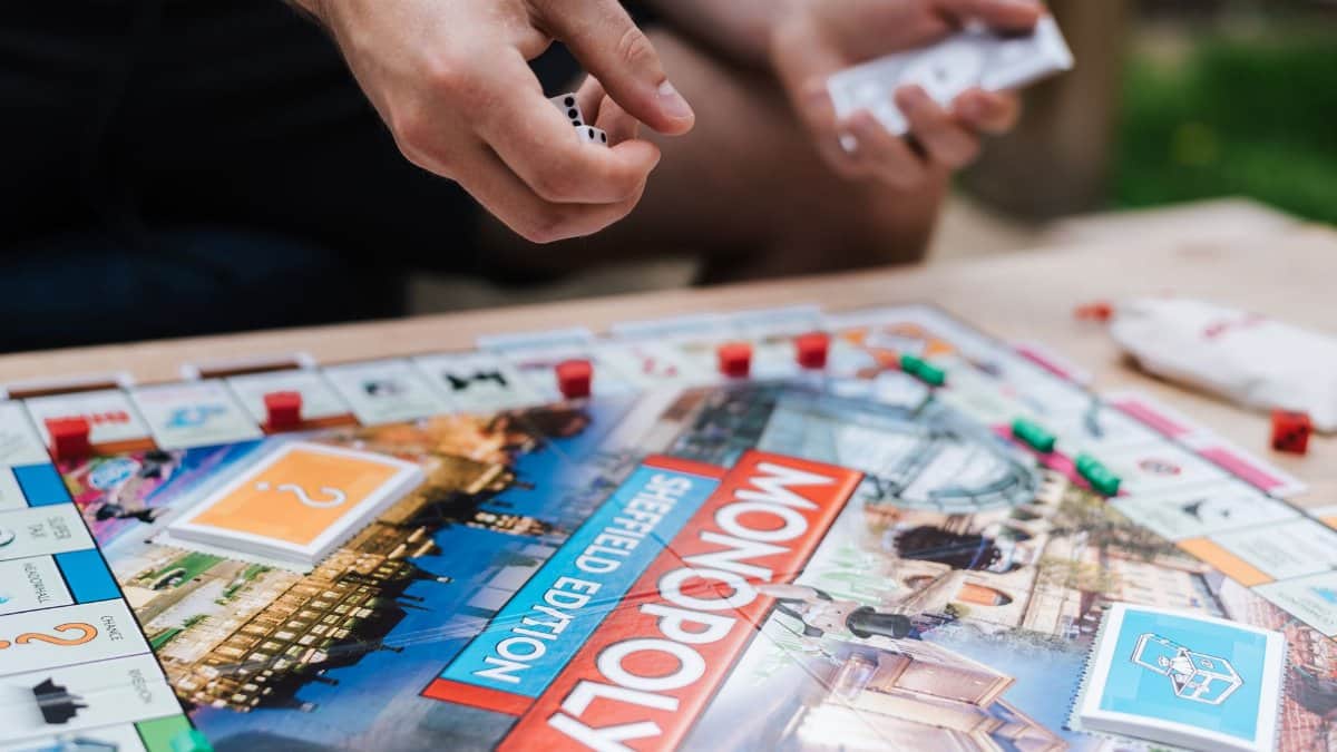 Crop anonymous male player with dices and fake money playing Monopoly at table with deed cards