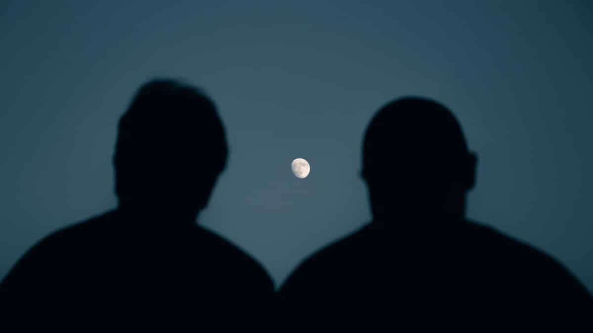 Two silhouettes gaze at the moon in a serene night sky over Mashhad, Iran.
