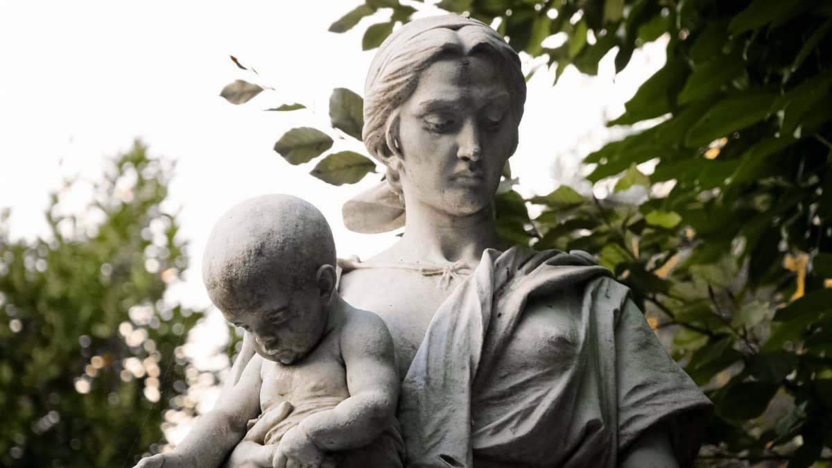 A detailed stone sculpture depicting a mother holding her child, surrounded by lush greenery.