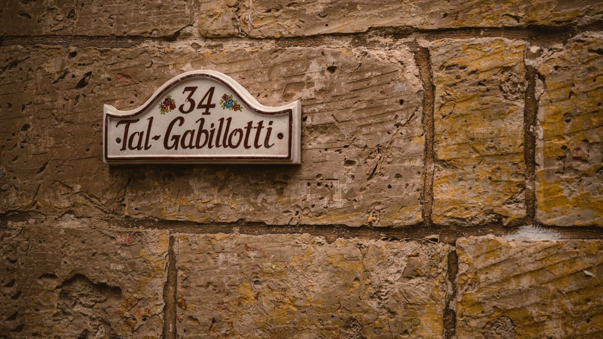 Ornate street name plaque 'Tal-Gabillotti' on rustic Maltese stone wall.
