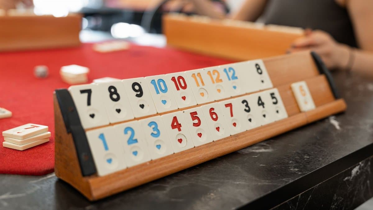 Colorful Rummikub tiles arranged on a wooden rack during an indoor game session.