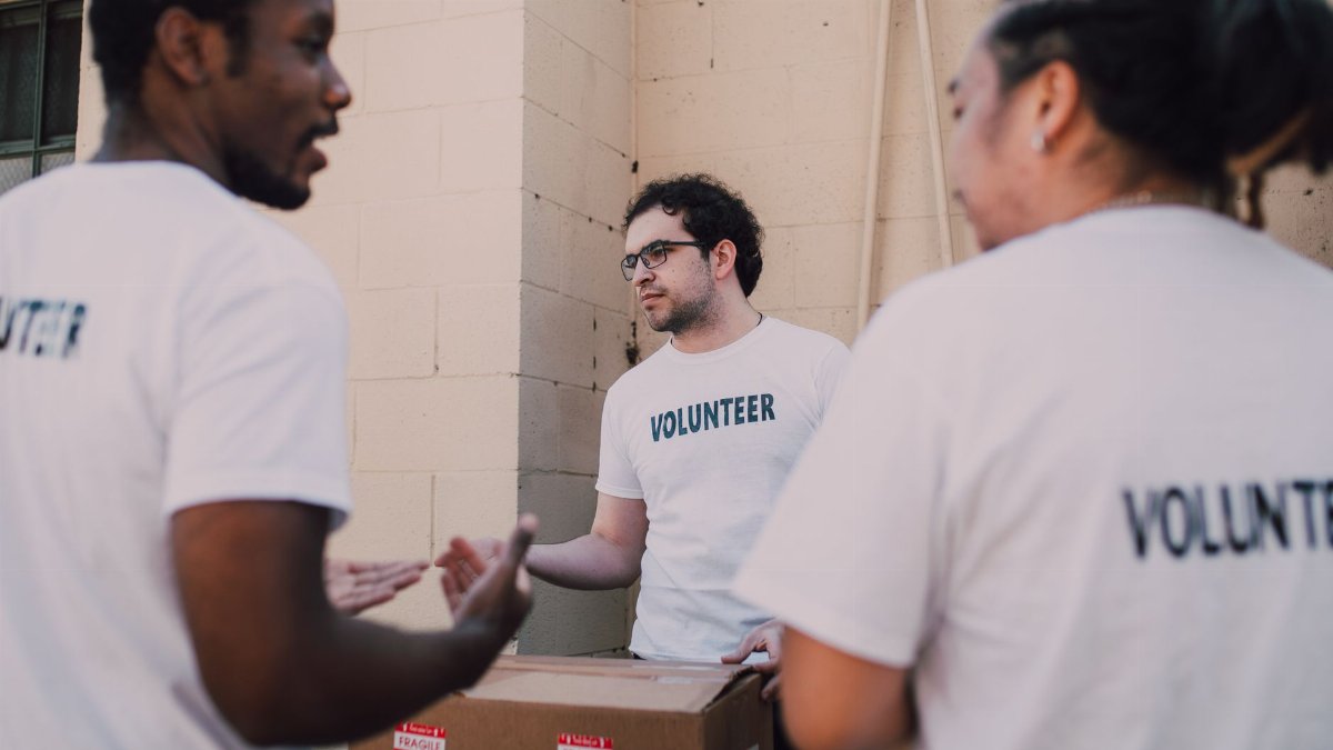 Group of diverse volunteers organizing food donations in white shirts marked with 'Volunteer'.