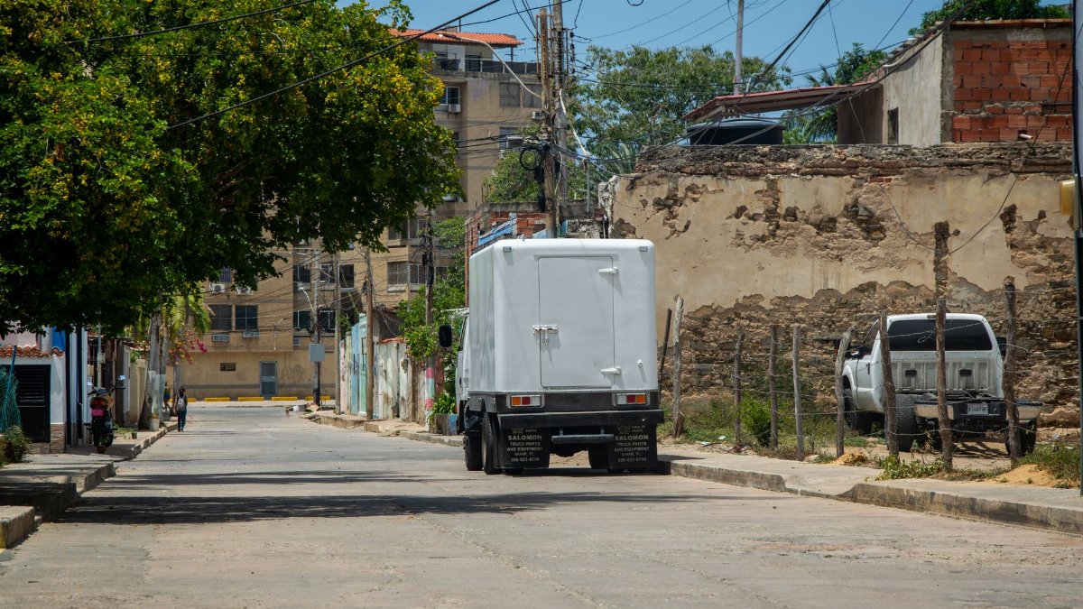 A city street scene featuring trucks, buildings, and green trees on a sunny day.