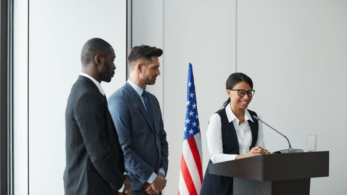 A diverse team in business attire at a podium with an American flag, showing unity and professionalism.
