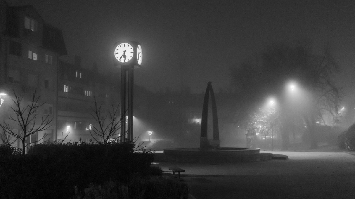 Foggy urban landscape with illuminated clock tower at night.