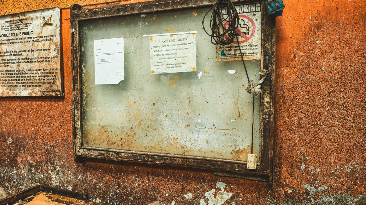 A rustic notice board with announcements on a textured orange wall in Dumaguete City, Philippines.