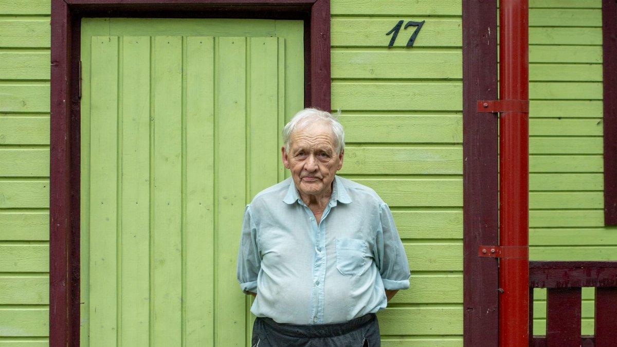 Senior man in front of vibrant wooden house in Tartu County, Estonia. Simple rural life portrait.