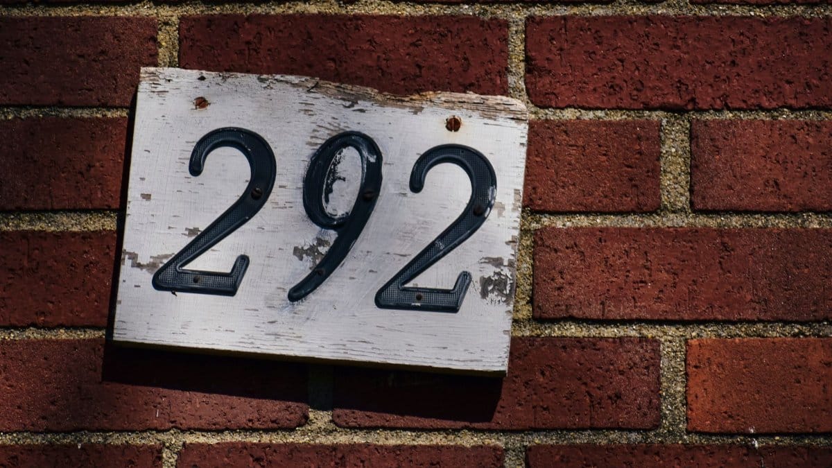 Close-up of a weathered house number 292 sign on a red brick wall, in sunlight.