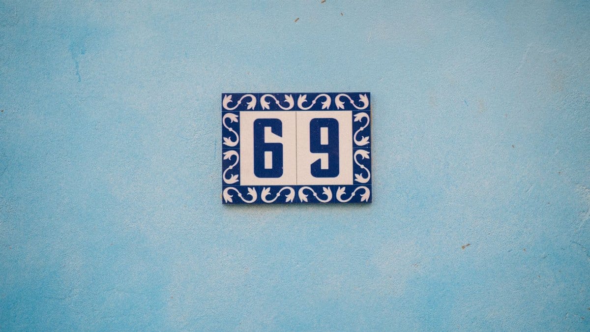 A stylish blue and white house number 69 on a textured blue wall.