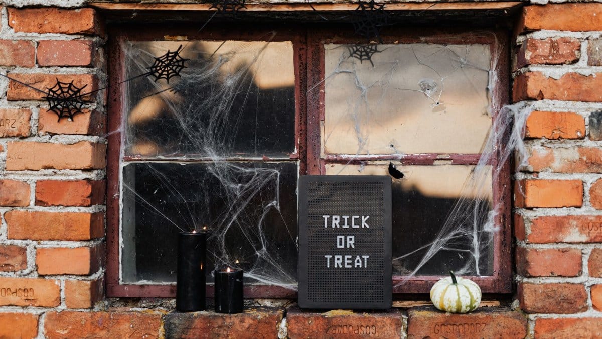 Spooky Halloween window decor with trick or treat sign, candles, and cobwebs.