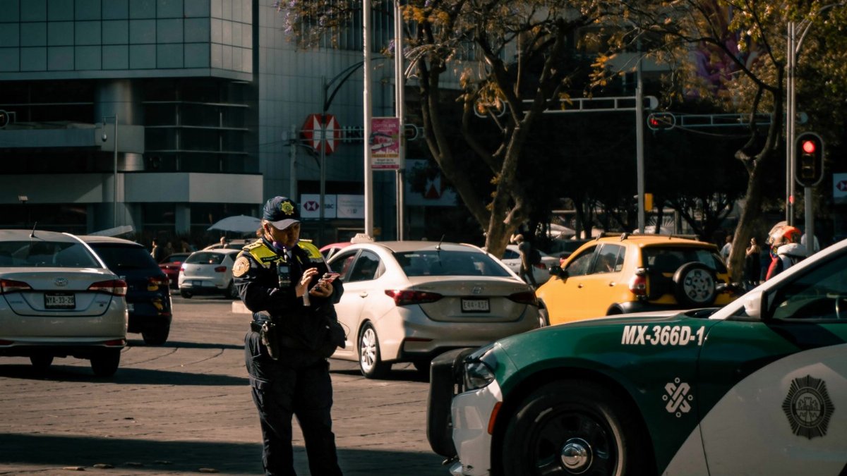 Policewoman in uniform ticketing a car in urban Mexico City setting.