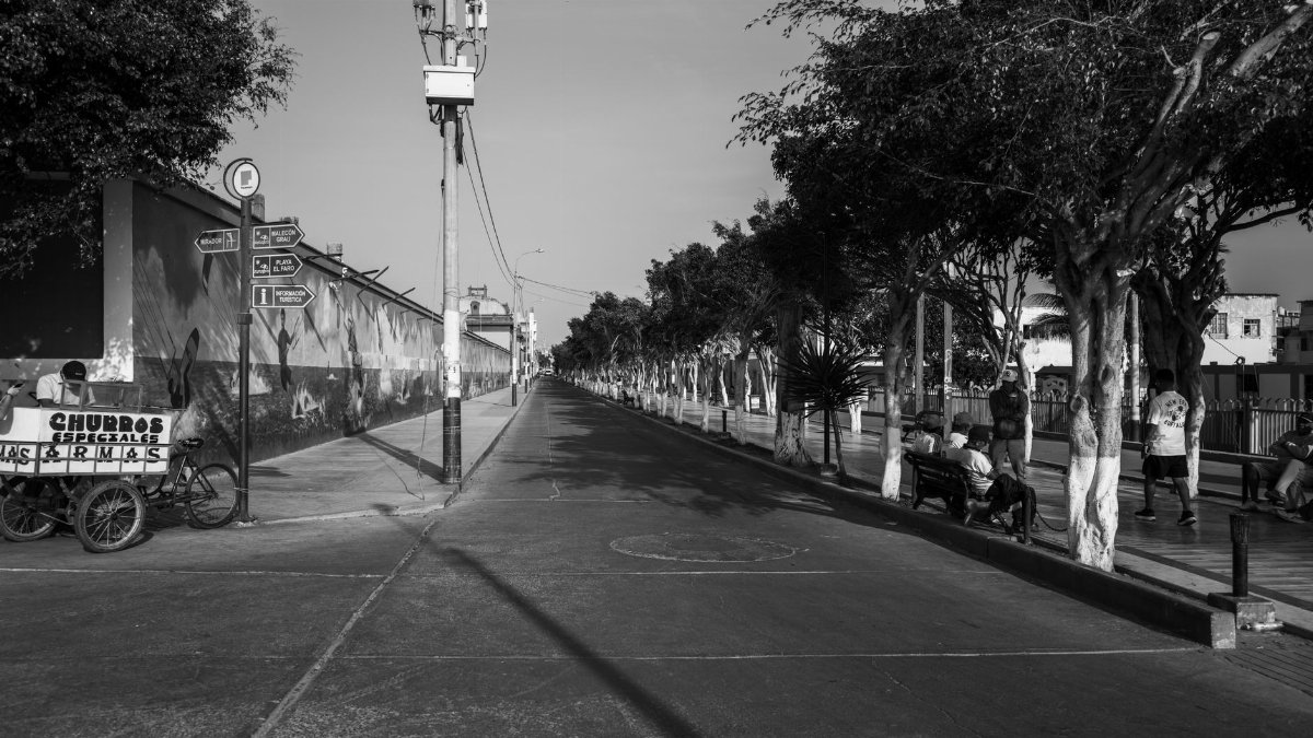 Black and white street scene with churros cart and people sitting in Pacasmayo, Peru.