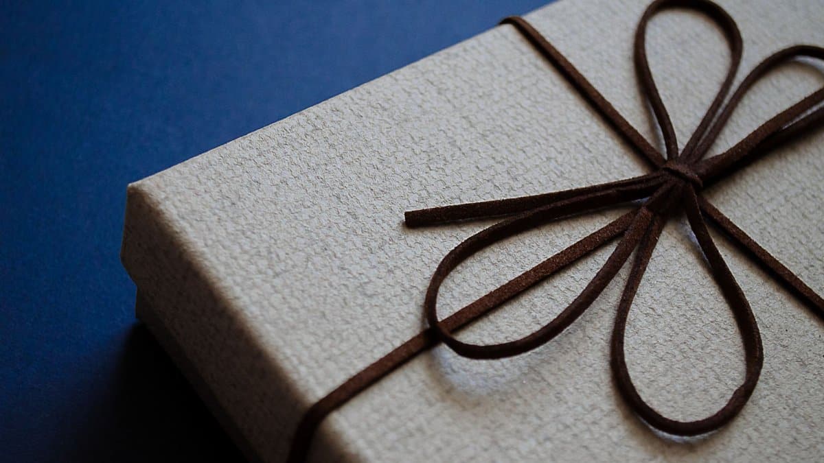 Close-up of an elegant gift box with a brown leather bow on a blue surface, perfect for special occasions.