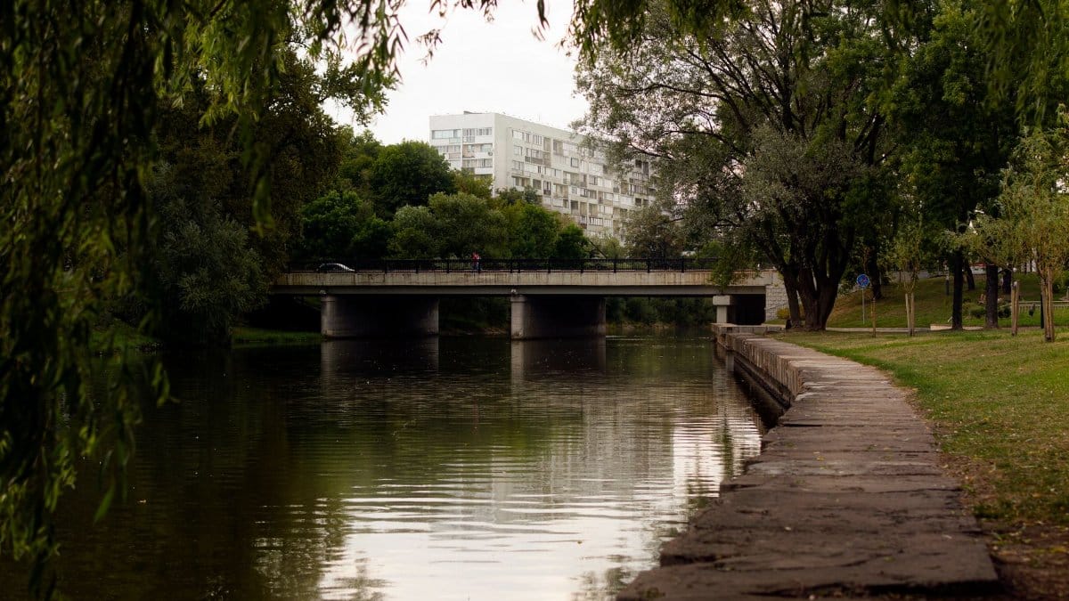 Peaceful view of a bridge over a river in a Minsk park with lush greenery.