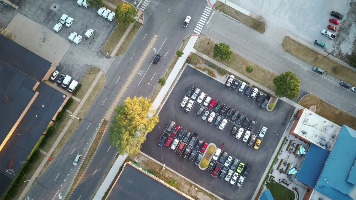 Drone shot of an urban parking lot and surrounding roads at daytime.