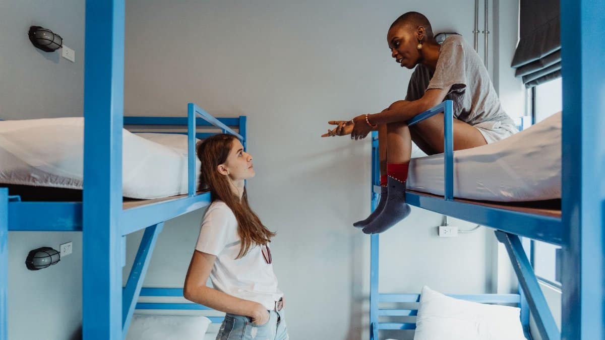 Two women engaging in conversation on bunk beds in a modern dormitory room.